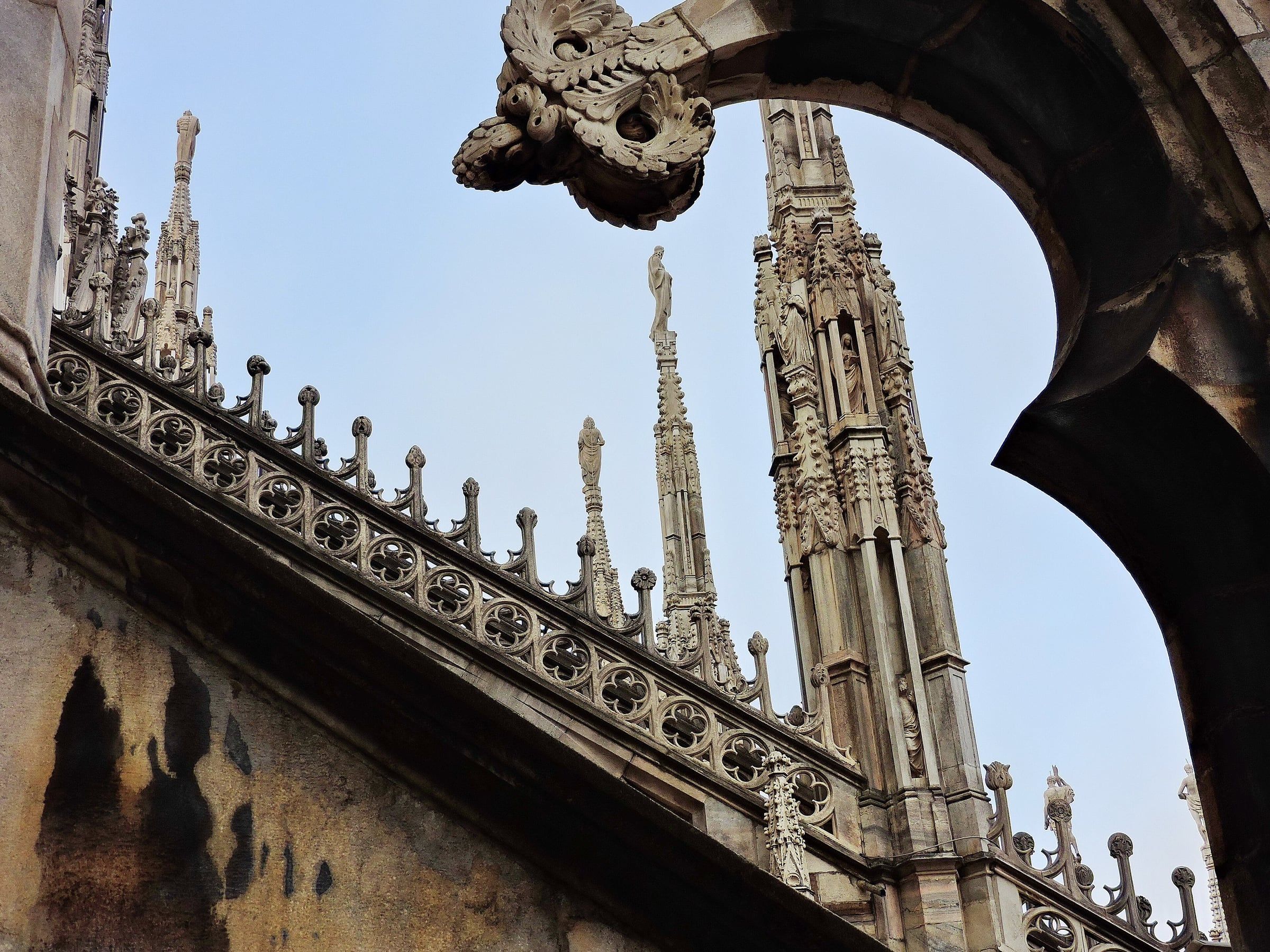 Carved marble spires and an openwork stone balustrade on a cathedral roof against a pale sky.