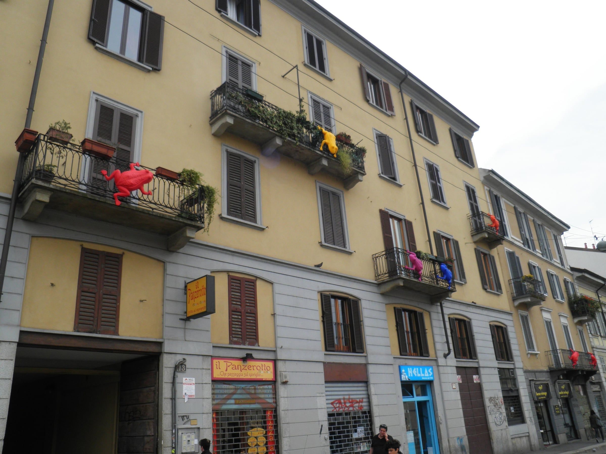 Street lined with tall balconied apartment buildings in yellow and grey, with a bright sky above.