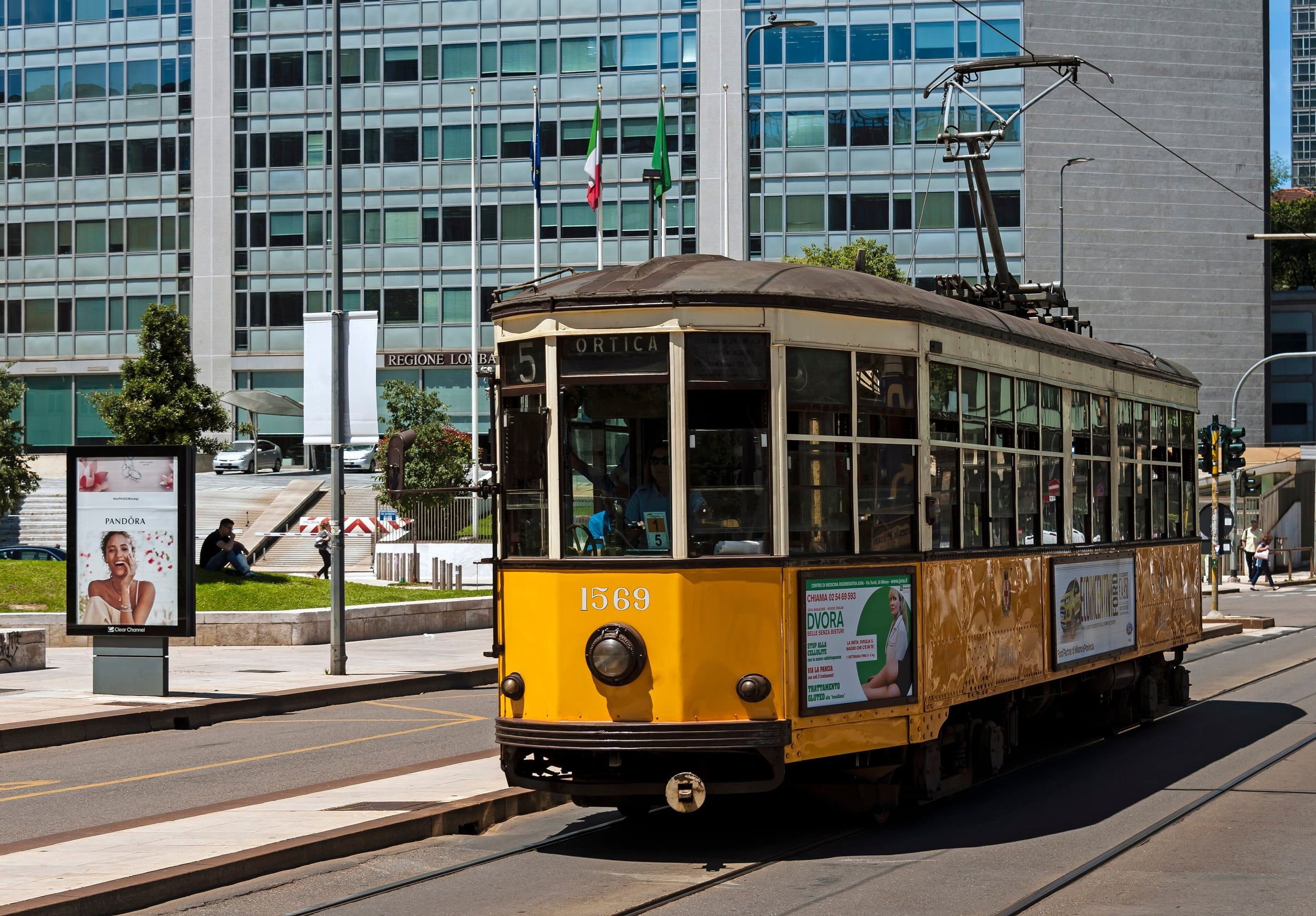 Vintage yellow tram running across a city square past tall glass-fronted buildings.